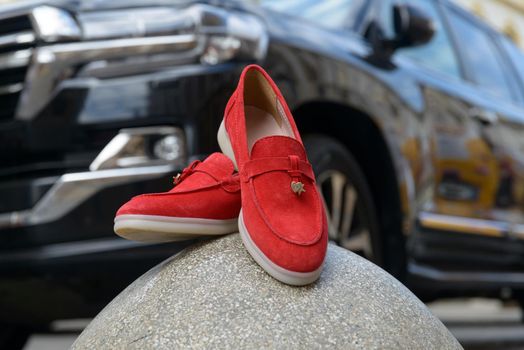 Woman's red stylish suede loafer shoes on a stone, car on a background. Pair of trendy female loafers shoes, outdoors