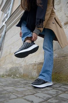 Stylish young girl posing. She is wearing a beige coat, jeans and stylish leather sports shoes.