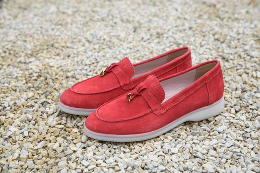 Woman's red stylish suede loafer shoes on the stone background. Pair of trendy female loafers shoes, outdoors.