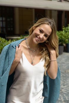 Fashionable young woman with blond hair dressed in beige dress and checkered coat posing. Street style.