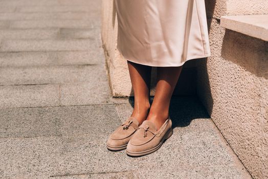 Portrait of fashionable women in beige dress and stylish suede loafer shoes posing in the street