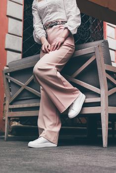 Stylish woman in fashion white sneakers shoes and beige trousers walks around the city. Close-up.