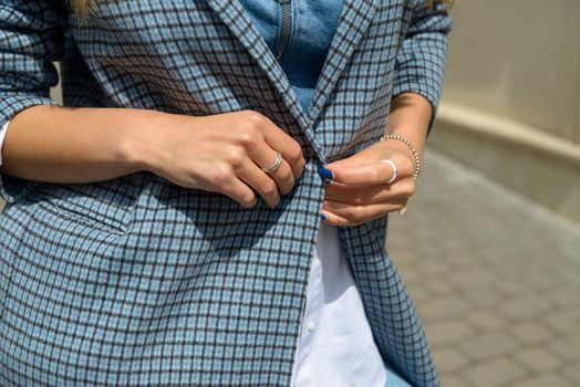 beautiful female tanned hands with blue manicure and element of stylish checkered coat