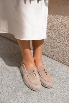 Portrait of fashionable women in beige dress and stylish suede loafer shoes posing in the street