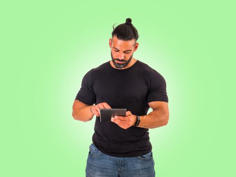 Attractive muscular man using electronic tablet, tapping on it, standing in studio shot