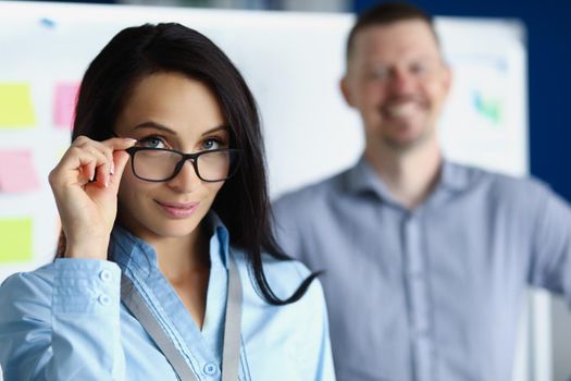 Portrait of pretty woman employee doing her glasses. Work as team on new project. Smiling male colleague on background. Company worker, business presentation, teamwork concept