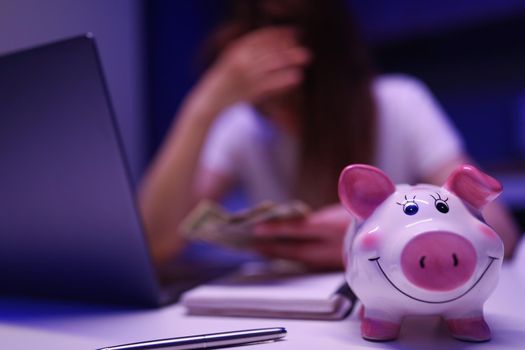 Close-up of piggy bank on desk, broken woman count money on background. Saving up for tomorrow, pay bills, invest. Finance, planning budget, economy, family banking concept. Blurred background