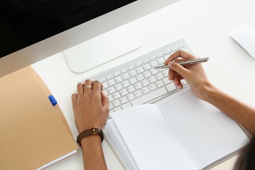 Top view of modern working place with laptop, keyboard, notebook. Woman typing and making notes in open diary. Copy space, mockup, workplace, office, technology, secretary concept