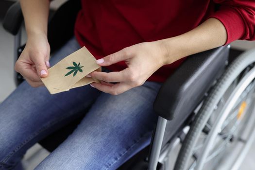 Close-up of woman hands holding package with hemp plant, person sit in wheelchair medication for treatment. Hope for faster healing. Alternative medicine, healthcare, disabled people concept