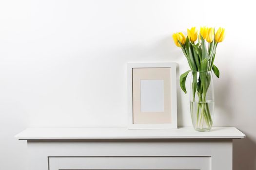 Bouquet of yellow tulip in the glass vase on white table