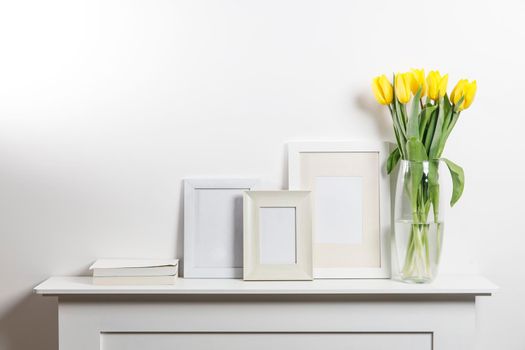 Yellow tulips in a glass vase and photo frames with space for inscriptions on a white chest of drawers