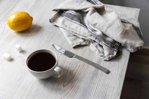 A cup of coffee, two pieces of sugar, a lemon on the table.