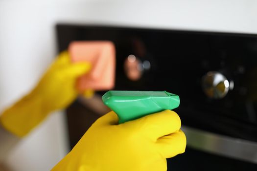 Close-up of woman housekeeper wiping dust from oven using spray and fabric, keep surface clean and shiny at home. Cleaning service job, cleanup, sanitizing, clean space concept. Blurred background