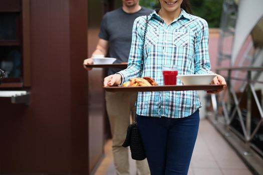 Portrait of friends going to eat takeaway food outside. Man and woman carry trays with lunch, break for eating in buffet. Fast food, hunger, picnic, friendship concept