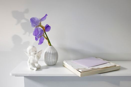 Blue iris in a corrugated vase with a piece of craft paper on a white table. Figurine of the angel. Place for text