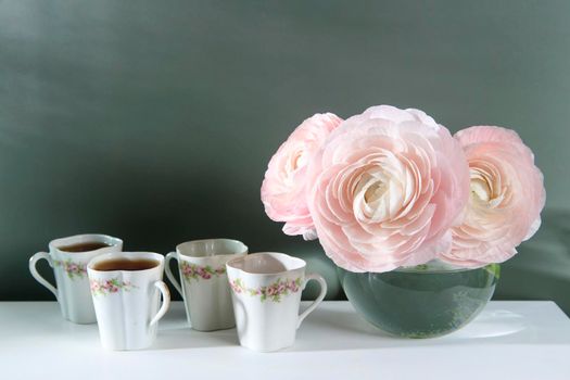 Three pale pink ranunculus in a transparent round vase on the white windowsill. Copy space. Place for text