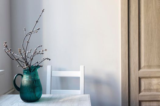 Cut branches of an apple tree in a green jug on a beige table in the kitchen