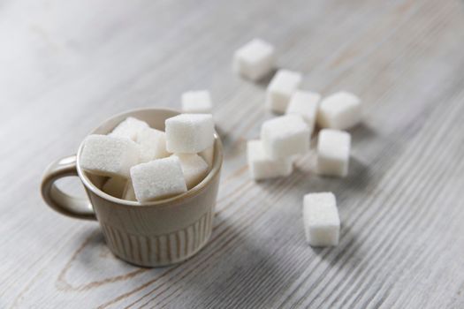 Cup with refined sugar in pieces scattered on the table