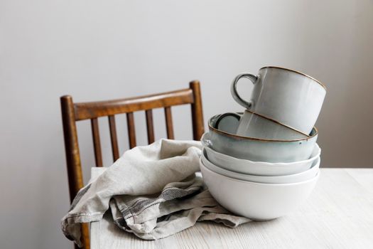 A pyramid of white bowls, plates and cups of different sizes and colors on a beige table in the kitchen. Scandinavian style. Place for your text. Copy space