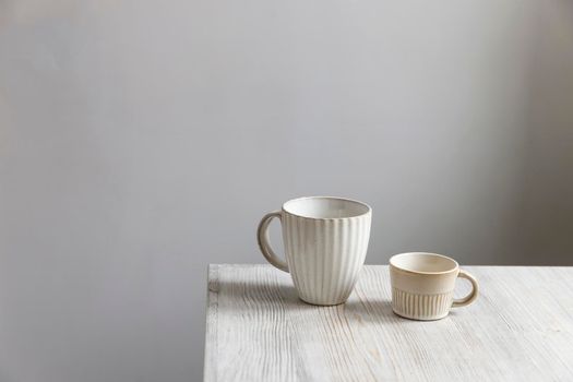 Two porcelain white cups are on the beige table. Large and small cup