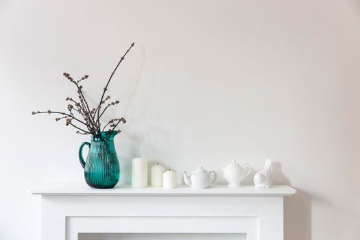 American maple branches in a green glass jar, porcelain cups, figurines, teapot on a white chest of drawers. Scandinavian style