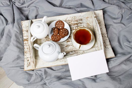 interior and home coziness concept. Top view. A cup of tea, a teapot with herbal tea, sugar bowl on a wooden white tray on the bed. Porcelain cup