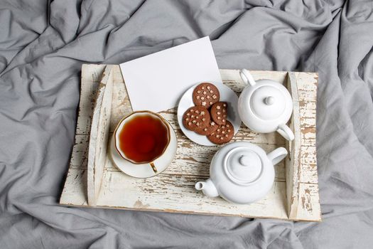 interior and home coziness concept. Top view. A cup of tea, a teapot with herbal tea, sugar bowl on a wooden white tray on the bed. Porcelain cup