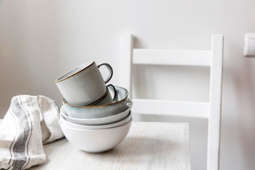 A pyramid of white bowls, plates and cups of different sizes and colors on a beige table in the kitchen. Scandinavian style. Place for your text. Copy space