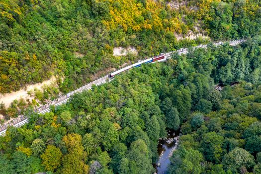 Train passes through a mountain near the river, aerial drone shot. 