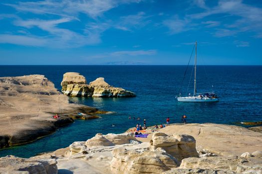 Yacht boat at famouse Sarakiniko beach white rocks tourist attraction with tourists on beach in Aegean sea on sunset, Milos island , Greece