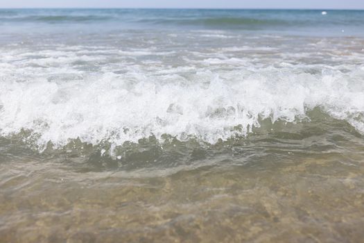 Close-up of blue sea waves, sandy coastline, choppy sea, clean water. People on horizon swimming in water. Beach, ocean, black sea, holiday, summer, relaxation concept