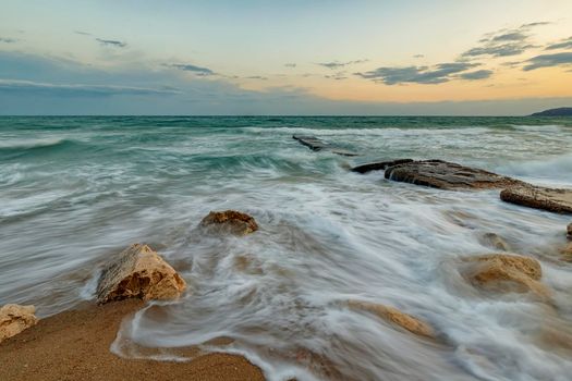 Amazing long exposure seascape with waves flowing between rocks at sunset