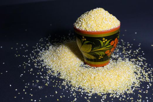 Raw corn grits flour in a wooden bowl on black background