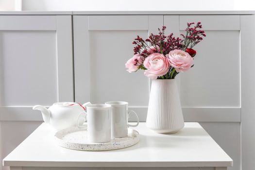 Bouquet of pink Persian buttercups on a white table in front of a chest of drawers. Scandinavian style. Place for text