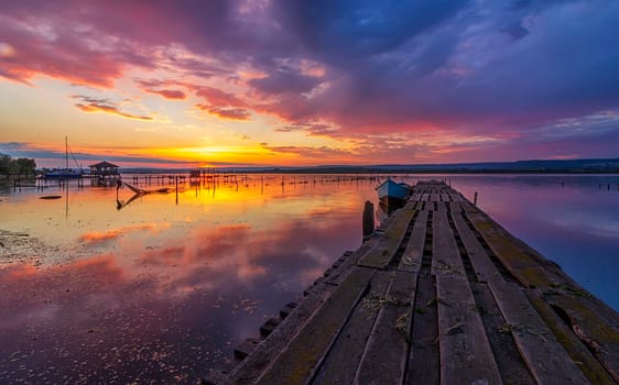 Amazing mood sunset at a lake coast with a boat at a wooden pier