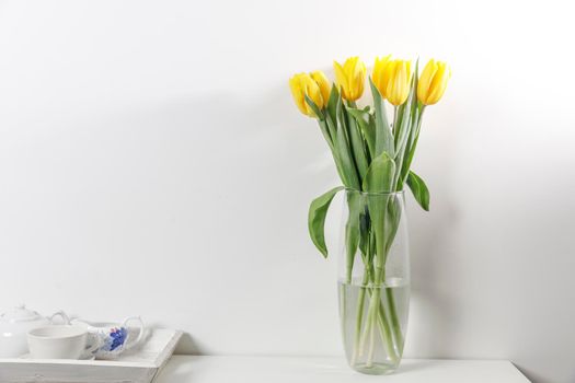 Bouquet of yellow tulip in the glass vase on white table