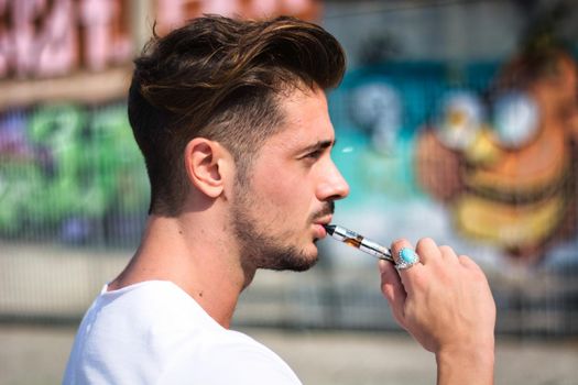 Handsome man smoking e-cigarette, vaping outdoor in city setting
