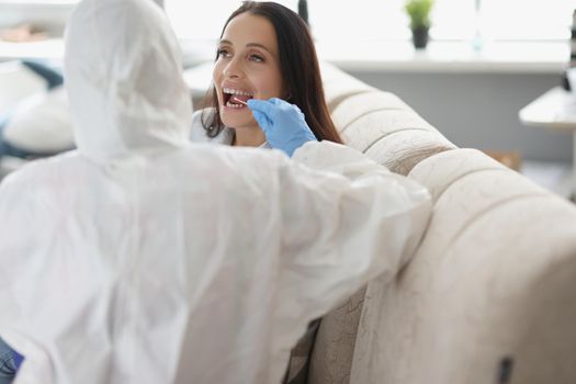 Portrait of doctor or laboratory assistant in protective suit takes swab from throat of sick patient, perform procedure at home, lab test for coronavirus. Quarantine, pandemic, health concept