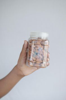hand holding a jar of almond nuts on white .