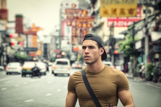 Muscular young handsome man walking on busy sunny street in Bangkok, Thailand.