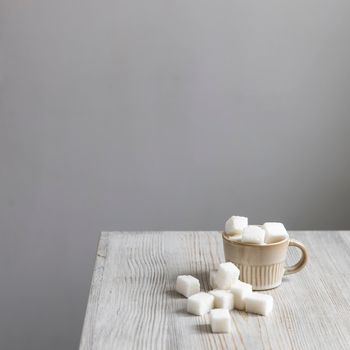 Cup with refined sugar in pieces scattered on the table