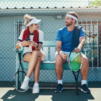 Full length shot of two young tennis players sitting down and having a conversation together outdoors on the court.