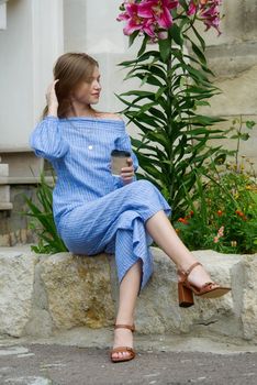 A female posing near flower on a stone curb wearing a striped jumpsuit. summertime