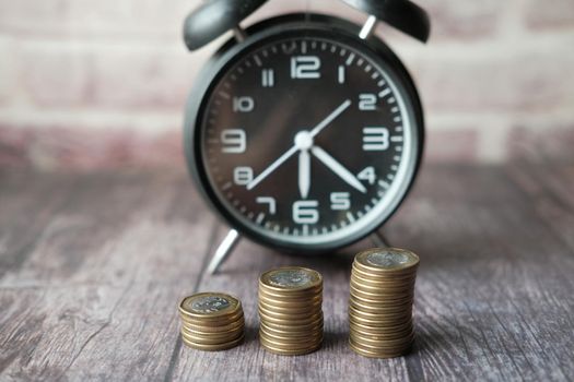 old alarm clock and stack of coins on table .