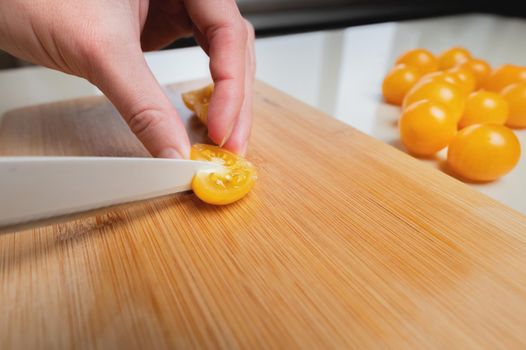Sliced yellow cherry tomatoes on a wooden board in shallow depth of field against the background of a bowl with veggie salad ingredients.