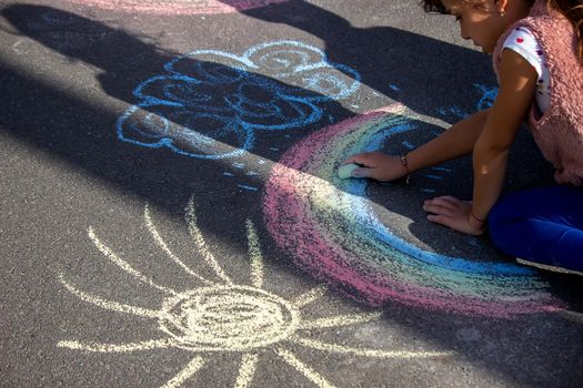 girl draws a rainbow, sun, car with chalk on the asphalt. Selective focus