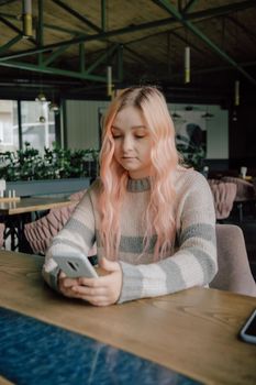Young curious woman with pink hair likes millennial beautiful girl looking with interest watching smiling lady sitting nearby in cafe using smartphone, flirt in public place, dating and love at first sight concept