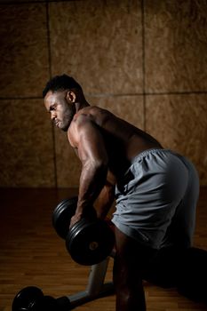 African american man with naked torso doing triceps row with dumbbell on bench