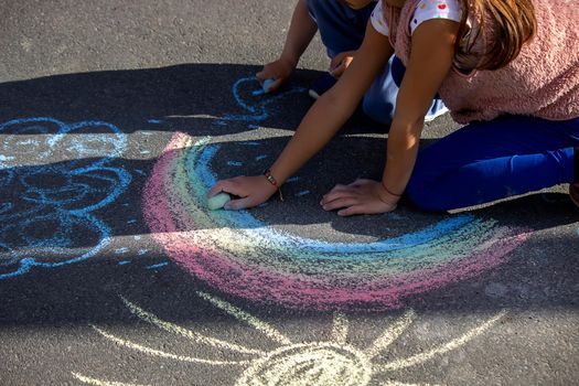 girl draws a rainbow, sun, car with chalk on the asphalt. Selective focus
