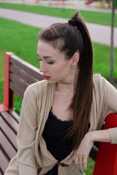 attractive brunette woman sitting on a bench in park. fashion clothes, stylish look.